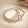 Detailansicht eines silbernen Schlangen-Federarmbands auf einer strukturierten Steinfläche - Silber