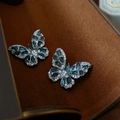 Primer plano de aretes de mariposa plateados con gemas azules sobre textura de terciopelo - Pendientes de botón (Par) / Azul