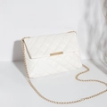 White quilted flap shoulder bag with gold chain strap and metal clasp in a minimal setting - White