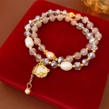 Detailansicht eines zweilagigen Perlenarmbands mit Saturn-Anhänger auf rotem Samt - Gold Rosa