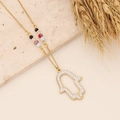 Detail der Hamsa-Hand Goldkette mit hohlem Umriss und bunten Perlen auf Goldkette - Hand der Fatima