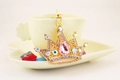 Detail of crown keychain with pink pear-shaped crystal on white coffee cup - Pink