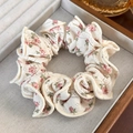 Detailed texture of cream knit hair scrunchie with pink floral patterns in a wooden tray - Beige Floral Knit Style