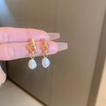 Dettaglio di orecchini a nodo dorato con perla barocca tenuti tra le dita - Nodo Bianco (Perla d'Acqua Dolce) (6# Silver Earring Post)
