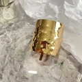 Detailed view of golden hammered texture bracelet resting on ice cubes with white paper - Gold