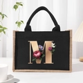Black canvas tote bag with golden letter M and floral print in a minimalist studio setting - Bronze Floral Letter M