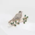 Gold-plated bird brooch featuring white rhinestones and green enamel leaf details - Gold Bird on Branch (241)