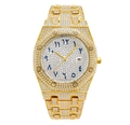 Detail of gold iced-out watch featuring octagonal bezel and blue Arabic numerals - Gold
