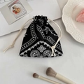 Dettaglio della borsa a coulisse paisley nera con cosmetici su una scrivania bianca - Paisley Nero