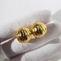 Orecchini a sfera dorati con texture a onde d'acqua tenuti in una mano con guanto bianco - Oro