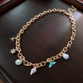 Detail of golden marine necklace featuring fishtail shell and pearl charms on wood background - Necklace - Gold