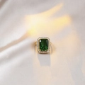 Elegant gold halo ring with emerald cut green gemstone on beige silk fabric - Emerald Green Ring (Gold)