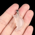 Hand holding a translucent pink quartz crescent moon pendant with carved face detail - Agate