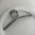 Close-up of silver metal hair claw clip with twisted streamlined design in a white tray - Grey Silver - Hanger Style
