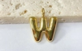 Detail of a golden puffed letter W pendant with a smooth metallic finish on a stone surface - Letter-W / Steel