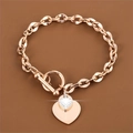 Détail d'un bracelet en acier inoxydable or rose avec doubles breloques cœur et fermoir T - Or rose