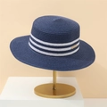 Detail of navy straw sun hat with white stripes and gold emblem on metal display stand - Navy Blue