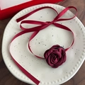 Primer plano de collar con rosa de tela burdeos y cintas en plato blanco decorativo - Estilo con Lazo de Cinta / Burdeos