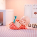 Sleeping monk ornament in red robe with ruyi scepter on pink checkered background - Lying Buddha Pose (Small Red)