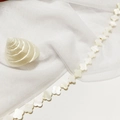 Close-up of pearl white clover-shaped natural shell bead on white mesh background - 14mm