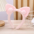 Detailed view of pink plush cat ear headband with soft pom-poms on a wooden table - Pink