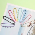 Eight colorful 6cm three-hole lacquered safety pins arranged in a fan shape on a desk - Multicolor