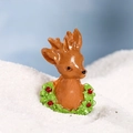 Miniature Christmas deer figurine with green wreath and red berries on white snow surface - Green Christmas Reindeer