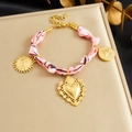 Detalle de pulsera dorada con pañuelo de seda rosa y colgantes de sol y corazón - Pulsera de Pañuelo de Seda Con Colgante de Moneda de Sol