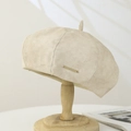 Detailed close-up of beige suede beret with a rectangular gold metal HiCrown plate - Suede / Beige