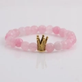 Facettiertes rosa Steinperlenarmband mit goldener Krone auf weißem Hintergrund - Facettierter Rosenquarz