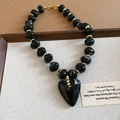 Macro detail of retro black heart pendant and gold bead accents on an acrylic necklace - Necklace / Black