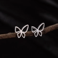 Primer plano macro de pendientes de mariposa huecos plateados sobre una rama - Color Acero