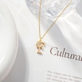 Detail shot of a golden letter F necklace with a zircon flower on an elegant white background - Letter F