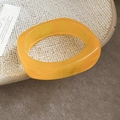 Detail van een geometrische oranje hars armband op een beige keramische schaal in retro stijl - Geel