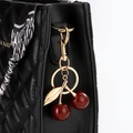 Détail d'un porte-clé cerise en résine pailletée avec attaches dorées sur sac matelassé - Bordeaux