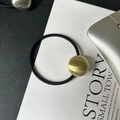Detail eines schwarzen elastischen Haargummis mit einer gebürsteten goldenen Metallkugel - Goldene Kugel