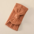 Macro detail of terracotta knitted baby headband with a large bow and soft cable stitch - Orange Red