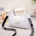 White quilted handbag with gold hardware and wide lettered shoulder strap in a lifestyle setting - White