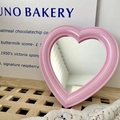 Pink heart-shaped vanity mirror with vintage plastic frame on a wooden surface - Pink