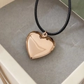 Primo piano di un medaglione a cuore dorato su cordino nero in una scatola regalo per gioielli - Ciondolo in acciaio inossidabile + corda nera / Oro rosa