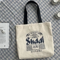 Detailed top view of beige canvas tote bag with artistic beer illustration on blue plaid cloth - Japanese Trendy Beige Bag