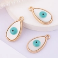 Macro shot of three teardrop-shaped white evil eye charms with golden frames for DIY jewelry - Water Drop