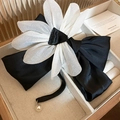Detail van een elegante zwarte satijnen strik haarklem met stoffen bloem en parelhanger - Zwart-wit strik bloem veerclip
