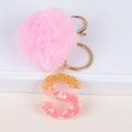 Close-up of pink pompom and gold foil resin letter S keychain on white background - Letter S