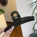 Close-up of a glossy black curved shark hair claw clip with golden metal spring detail - Translucent Grey Green