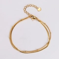 Dettaglio di un bracciale a doppio strato in oro con ciondolo a cuore e piccole perline - Oro