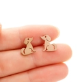 Detailed close-up of rose gold stainless steel puppy silhouette stud earrings on a finger - Sitting Dog (682) / Rose Gold