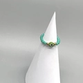 Detail of turquoise beaded stretch ring with green evil eye charm on a white stand - Adult Diameter 17-18mm / Green-Gold