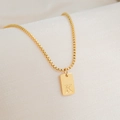 Close-up of gold 18K plated square letter K pendant on a box chain over white silk - Letter K