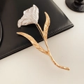 Détail d'une broche tulipe bicolore avec pétales argentés posée sur du cuir noir élégant - Or Blanc